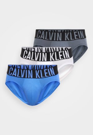 Three Calvin Klein men's briefs in blue, white, and grey with black waistbands and large Calvin Klein logo.