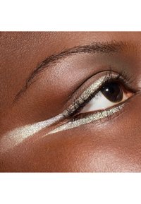 Gros plan sur un œil brun foncé avec un eyeliner métallique doré et argenté appliqué en une bande diagonale audacieuse. Les détails des cils sont visibles.