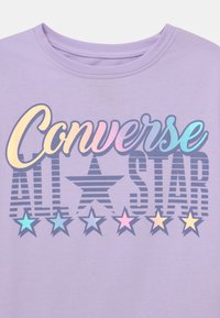 Fialové tričko s krátkým rukávem, ozdobené vícebarevným grafickým designem "Converse ALL STAR" se hvězdami v pastelových tónech. Hladká bavlněná textilie, kulatý výstřih.
