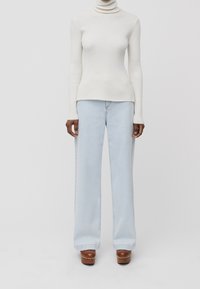 Col roulé blanc côtelé, silhouette ajustée. Jean bleu clair à jambes larges. Sabots marron ornés de clous argentés. Design simple et épuré avec un minimum de détails.