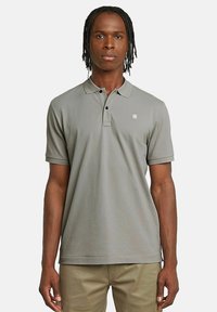 Szara koszulka polo z kołnierzykiem, krótkimi rękawami i subtelnym logo na piersi. Wykonana z gładkiego materiału o luźnym kroju.