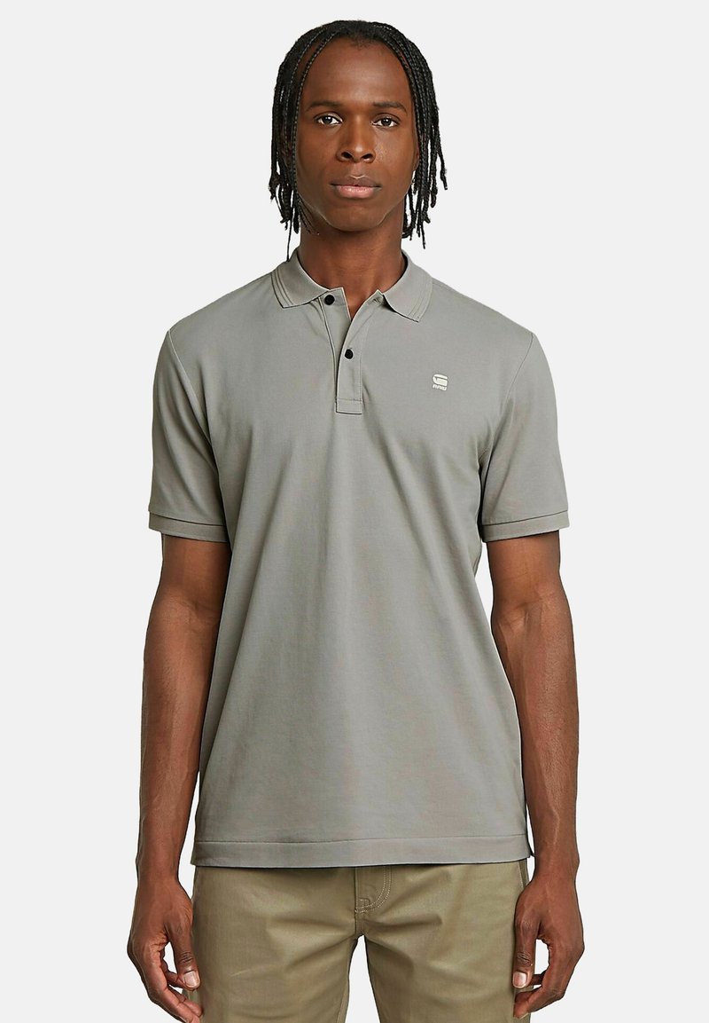 Szara koszulka polo z kołnierzykiem, krótkimi rękawami i subtelnym logo na piersi. Wykonana z gładkiego materiału o luźnym kroju.