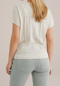 Pull beige clair à manches courtes avec texture côtelée et détails de coutures latérales, associé à un pantalon ajusté vert clair.