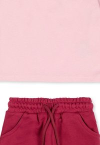 T-shirt en coton rose exposé au-dessus d'un pantalon de jogging bordeaux avec une taille élastique et des poches latérales, présentant une texture lisse.