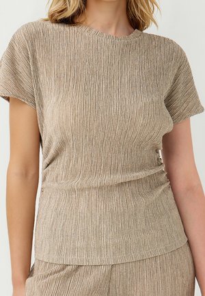 Vrouw draagt een beige geribd kort mouwtopje en bijpassende onderdelen met een getextureerd, geplooid stofontwerp.