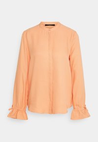 Blouse pêche à manches longues avec boutons dissimulés sur le devant, encolure ronde et poignets froncés noués avec de petits nœuds.