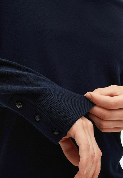 Marineblauer Strickpullover mit geripptem Bündchen, ausgestattet mit drei schwarzen Knöpfen am Handgelenk. Das Material wirkt glatt und strukturiert.