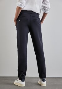 Navy jogger pants made of soft, stretchy material, featuring back pockets and tapered legs, paired with white sneakers.