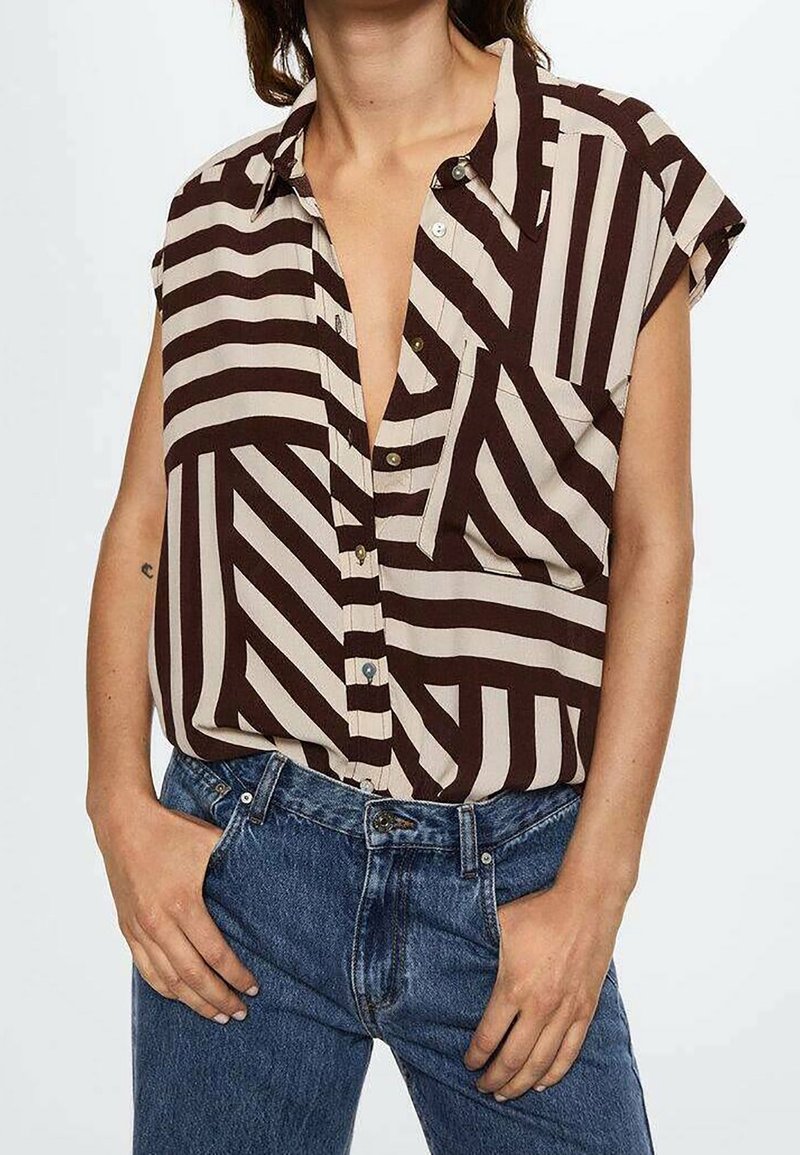 Chemise à manches courtes avec un motif géométrique brun et beige, dotée d'une fermeture à boutons et d'une poche poitrine. Le tissu semble lisse.