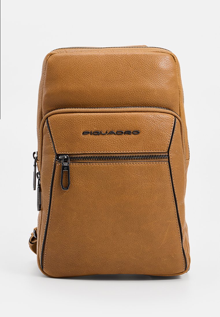 Zaino in pelle marrone con finitura testurizzata, tasca frontale con zip e logo embeddato nella parte superiore. Forma rettangolare compatta con zip laterale.