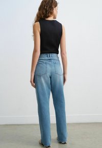 Jeans de talle alto de color azul claro con textura deslavada, que presentan dos bolsillos traseros y un dobladillo deshilachado. Combinados con una camiseta sin mangas negra.