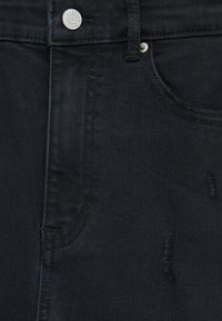 Gros plan sur l'avant d'un jean en denim noir avec un bouton en métal et des détails de poche avant, montrant des zones de tissu subtilement usées.