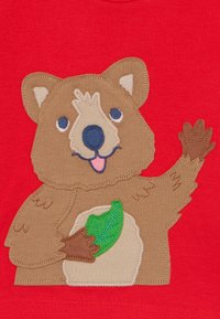 Camiseta roja con una aplicación de un oso pardo que lleva una hoja verde, una cara sonriente y detalles marrones en sus patas y orejas.