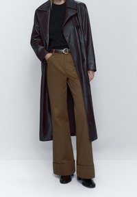 Brown leather long coat with a notched collar, paired with a black sweater and brown wide-leg trousers. Black shoes complete the outfit.