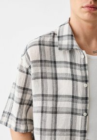 Lyhythihainen ruudullinen paita valkoisena ja mustana, jossa on napitettava etuosa, teksturoitu kangas ja klassinen levitettävä kaulusdesign.