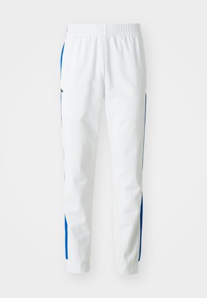 Pantaloni da jogging bianchi con strisce laterali blu. Presentano una vita elasticizzata e polsini aderenti. Realizzati in materiale sintetico liscio.