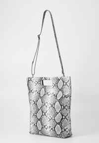 Black and white snake-patterned tote bag with a flat shape, a single strap, and a rectangular cutout handle. Smooth texture and synthetic material.