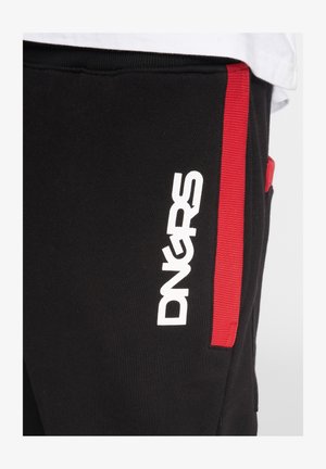 Fekete sportnadrág, amelynek oldalán egy fehér "DNGRS" logó található, valamint egy függőleges piros díszcsík és zsebet is tartalmaz a bal combon.