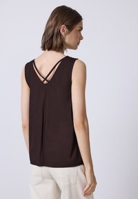 Haut sans manches marron avec un décolleté en V et des bretelles croisées à l'arrière. Fabriqué en tissu doux, il présente une coupe décontractée et un ourlet droit.