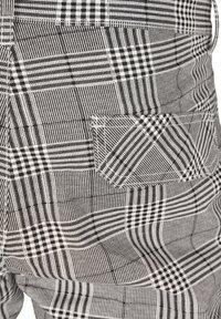 Gros plan sur un tissu à carreaux noir et blanc avec une poche cousue sur un pantalon ou une jupe.