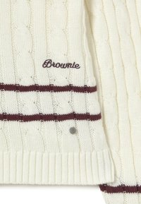 Suéter de punto trenzado crema con dos rayas horizontales marrón oscuro, bordado de "Brownie" y una pequeña etiqueta metálica redonda con una "B."