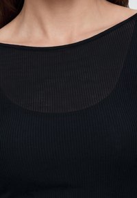 Κοντινό πλάνο ενός ατόμου που φοράει μαύρο ριμπ μπλούζα με διαφανές ντεκολτέ που αποκαλύπτει το πάνω μέρος του στήθους και την περιοχή της κλείδας.