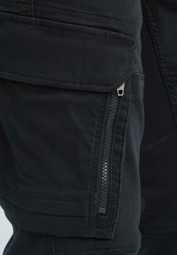 Schwarze Cargo-Hosen mit einem Reißverschlussfach, das über eine glatte Textur und ein kantiges Design verfügt. Enthält mehrschichtige Taschen und subtile Nähedetails.