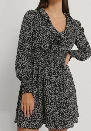Czarna sukienka w kwiaty z długimi rękawami, z marszczoną talią, falbanianym dekoltem i białym kwiatowym nadrukiem, wykonana z lekkiego materiału.