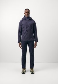 Navy waterproof jacket with hood, featuring zippered pockets and adjustable cuffs, paired with matching pants and textured hiking shoes.
