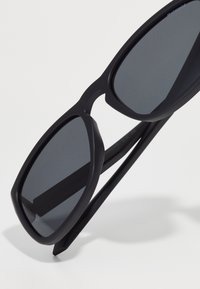 Ochelari de soare negri cu rame mari și rectangulare, lentile gri închis și un finisaj mat. Brațele sunt ușor conice și prezintă o textură netedă.
