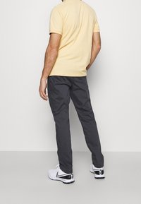 Man wearing a pale yellow short sleeve polo shirt, dark gray pants, and white Nike sneakers facing away against a plain light background.