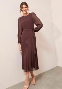 Langes, plissiertes burgunderfarbenes Kleid mit durchsichtigen langen Ärmeln und einem Bindegürtel. Der Stoff wirkt leicht und hat eine glatte Textur.