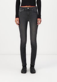 Jeans skinny negros con un acabado desgastado, diseño de cinco bolsillos y herrajes metálicos. Combinados con un suéter corto negro con acentos rojos.