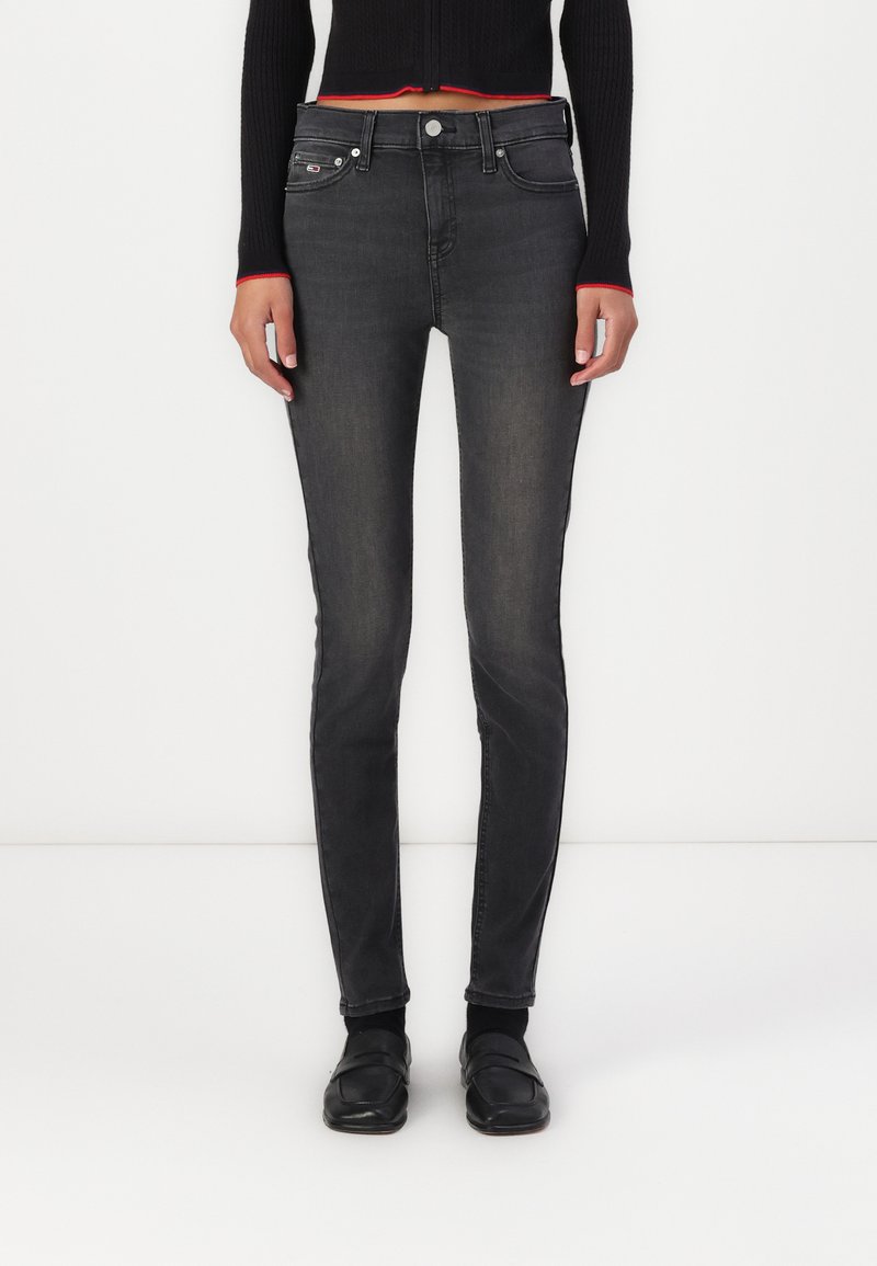 Jeans skinny negros con un acabado desgastado, diseño de cinco bolsillos y herrajes metálicos. Combinados con un suéter corto negro con acentos rojos.