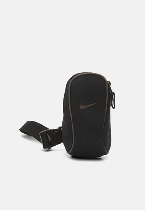 Kleine schwarze Bauchtasche mit Reißverschluss und verstellbarem Riemen, mit braunem Nike Swoosh-Logo auf der Vorderseite.