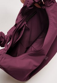 Bolsa morada hecha de materiales reciclados, con una textura suave, un bolsillo interior con cremallera y una apertura fruncida para un fácil acceso.