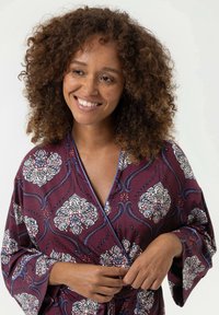 Bordeaux gekleed met een patroon van bloemen, met een zachte textuur, brede mouwen en een striksluiting, benadrukt door blauwe accenten.