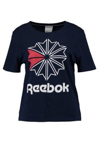 Námořnická modrá bavlněná tričko s velkým bílým a červeným geometrickým designem a nápisem "Reebok" v tučném bílém písmu na přední straně. Kulatý výstřih, krátké rukávy.