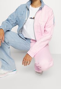 Dvoudílná tepláková souprava obsahující světle modrou denimovou bundu a růžové kalhoty. Bunda má zipové zapínání a šňůrky na límci.