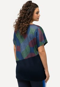 Top de manga corta con una parte superior de patrones coloridos en azul, verde y rojo, y una sección inferior lisa en azul marino, con una textura de tela suave.