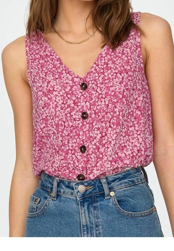 Ärmelloses, blumiges Oberteil in Pink mit weißen und hellrosa Mustern, verfügt über einen V-Ausschnitt und schwarze Knöpfe vorne, kombiniert mit blauen Jeans.
