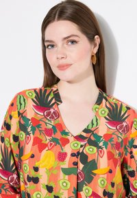Camicia colorata con motivo di frutta. Presenta fragole, banane, kiwi e angurie su uno sfondo arancione. Tessuto soffice con scollo a V.