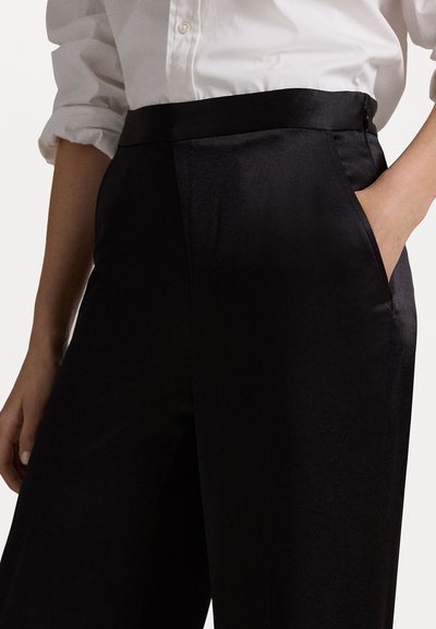 Μαύρο σατέν παντελόνι με λεία υφή, ψηλή μέση, μπροστινές τσέπες και κομψή εφαρμογή, συνδυασμένο με λευκό πουκάμισο με κουμπιά.