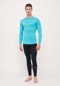 Blå langærmet træningsskjorte med rund hals, kombineret med sorte tætsiddende leggings. Begge dele har diskret Nike-logo.