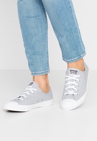 Szare płócienne trampki z niskim designem, białymi gumowymi podeszwami i sznurowanym zapięciem. Zawierają logo marki na języku i metalowe oczka.