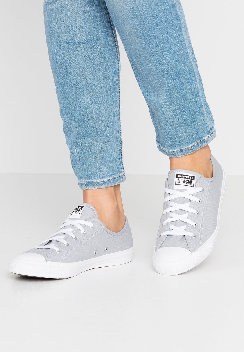 Szare płócienne trampki z niskim designem, białymi gumowymi podeszwami i sznurowanym zapięciem. Zawierają logo marki na języku i metalowe oczka.