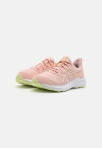 Baskets de sport rose clair en matériau mesh, avec des accents jaunes, un col rembourré et une semelle intermédiaire blanche. Semelle extérieure en caoutchouc vert texturé pour une meilleure traction.