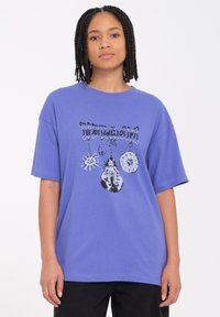 Camiseta de algodón morada de manga corta con estampado gráfico de un sol, un signo de paz, un reloj y una muñeca en la parte delantera. Diseño de corte relajado.