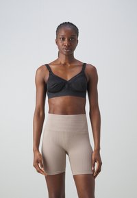 Svart, polstret bh med v-formet utringning og justerbare stropper, kombinert med høyt liv, ribbestrikkede beige shorts. Glatt tekstur.
