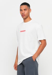 White cotton t-shirt with short sleeves, featuring a red "QUIKSILVER" logo on the chest. Casual fit, minimalistic design.